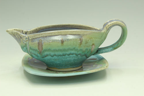 Ceramic gravy boat with handle on a matching saucer against a light background