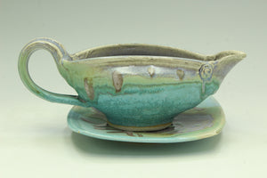 Green ceramic gravy boat with a matching saucer on a light gray background