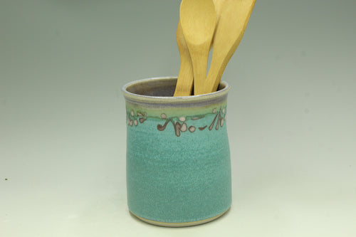 Turquoise ceramic utensil holder with wooden spoons on a gray background