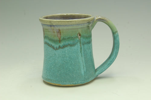 Turquoise ceramic mug with a green rim on a light gray background
