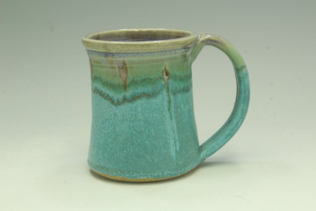 Turquoise ceramic mug with a green rim on a light gray background