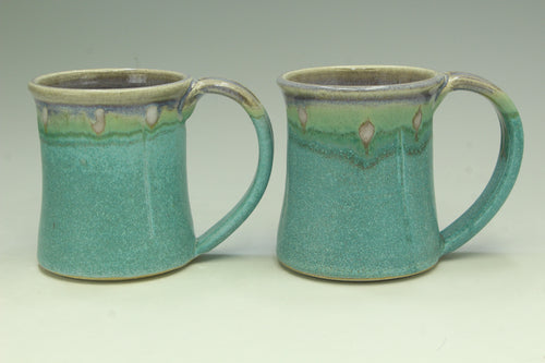 Two turquoise ceramic mugs with green accents on a light gray background