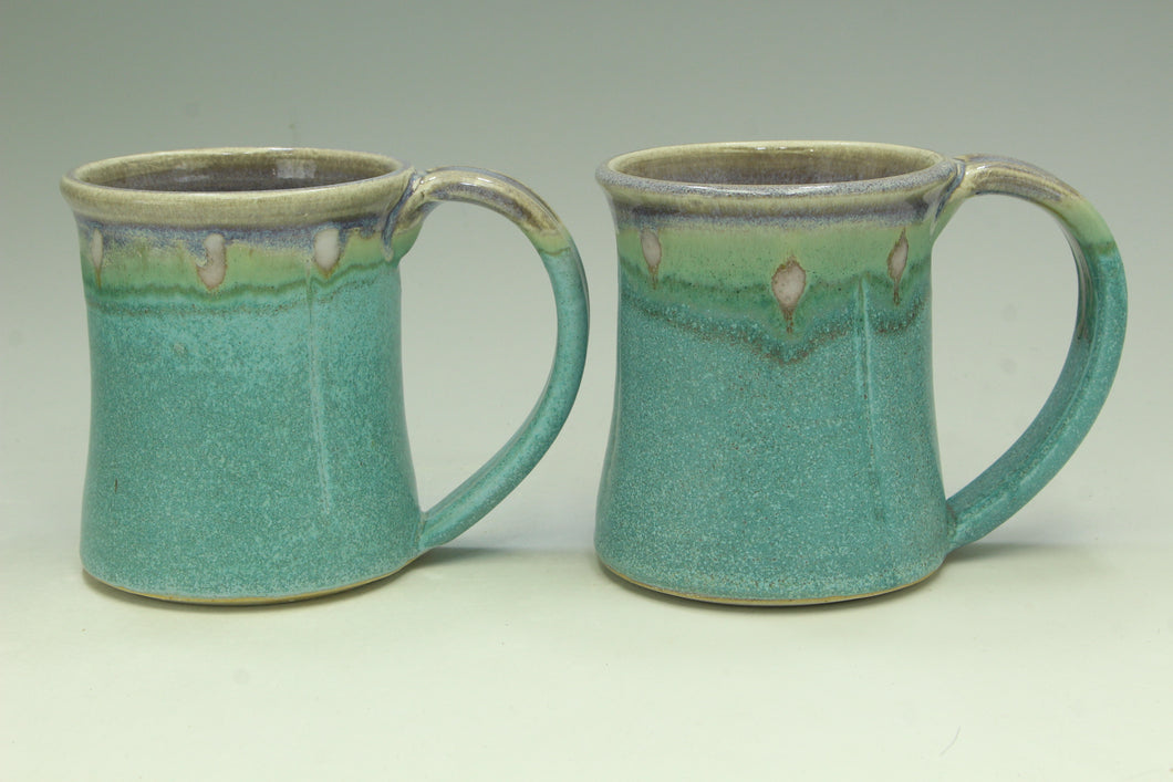 Two turquoise ceramic mugs with green accents on a light gray background
