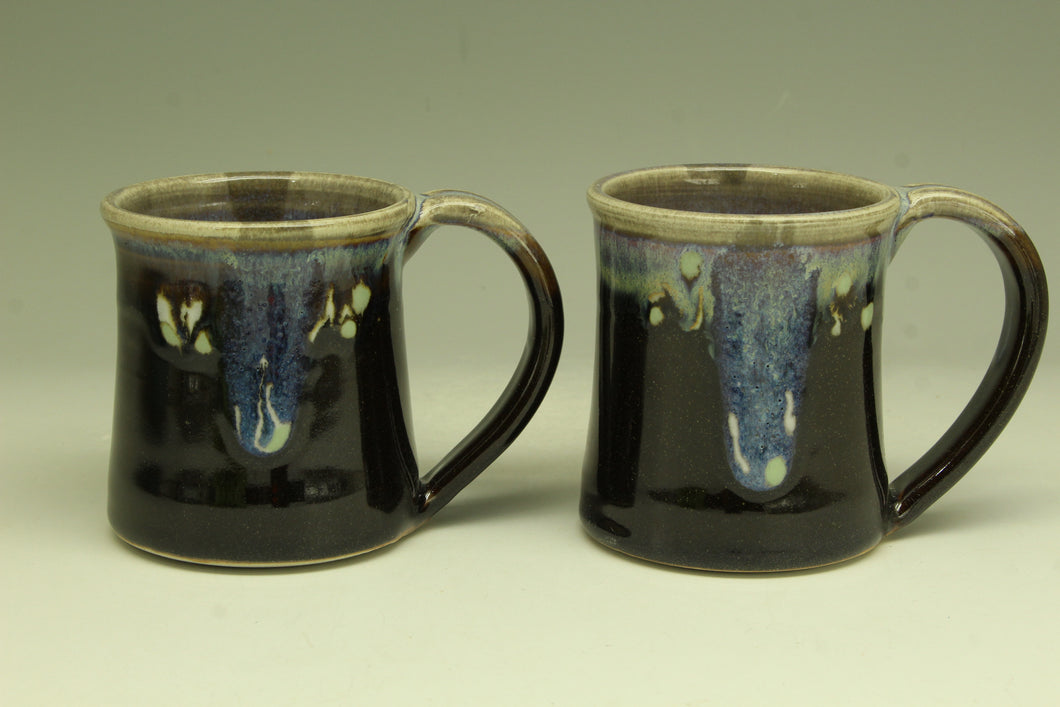Two black ceramic mugs with a glossy finish on a light gray background