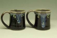 Load image into Gallery viewer, Two black ceramic mugs with handles on a beige background
