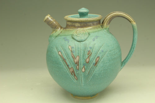 Turquoise ceramic teapot with decorative elements on a beige background