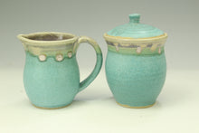 Load image into Gallery viewer, A ceramic pitcher and matching lidded jar with a speckled turquoise glaze, set against a neutral light gray background.